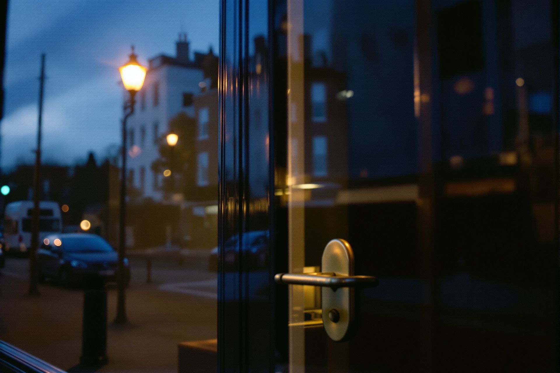 A small office seen in reflection in its own glass front door at dusk, the brass handle in focus