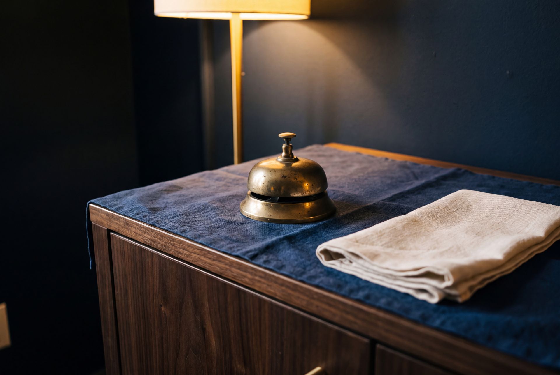 A brass bell and a folded cloth on a navy blotter under a lamp