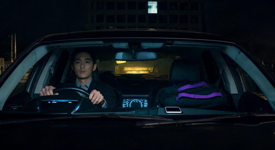 A business owner sits alone in a parked car outside an office building at night, hands still on the steering wheel, using AI as a thinking partner while the phone rests face-down on the passenger seat.