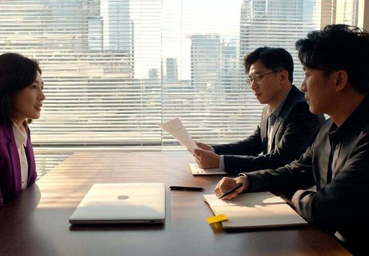 Three people in business attire sit at a conference table in an office with large windows; two interviewers face a candidate, preparing to discuss B2B client AI data security questions.