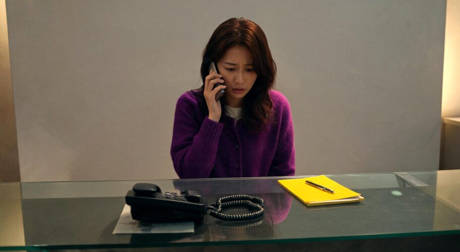 A small business owner considering AI automation vendor escrow while standing at a reception counter after hours, holding a mobile phone to one ear and looking at a desk phone with its cable unplugged on the counter.